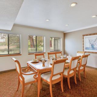 A well-lit dining room featuring a large table with eight chairs, surrounded by windows and adorned with artwork on the wall.