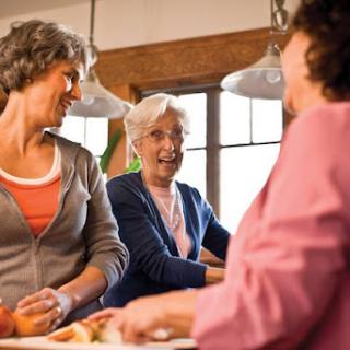 A joyful gathering of women sharing laughs and cooking in a cozy kitchen.