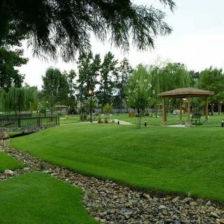 A scenic park featuring lush green grass, a small gazebo, and a variety of trees.