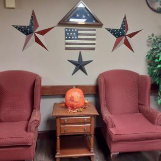 A cozy seating area with patriotic wall decor and a festive pumpkin on a wooden table between two red chairs.