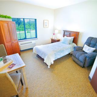 A cozy and well-lit bedroom with a single bed, chair, and window view.