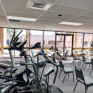 A spacious gym area with various exercise equipment including treadmills and stationary bikes, accompanied by several chairs near large windows.