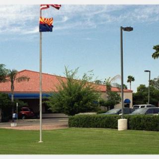A view of a building with flags and palm trees, alongside a parking lot under a clear sky.