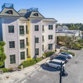 A modern three-story residential building with parking and clear blue skies.