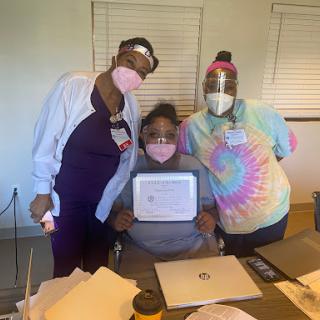 A group of three individuals in healthcare attire celebrating a achievement with a certificate.