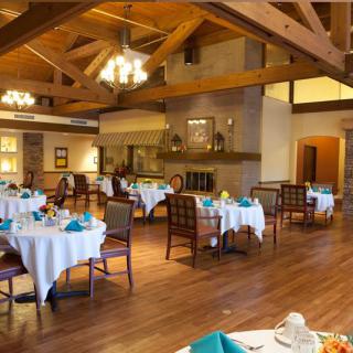 A cozy restaurant dining room with neatly arranged tables and chairs, wooden ceilings, and elegant chandeliers.