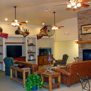 A cozy rustic living room with leather sofas, a fireplace, and ceiling fans.