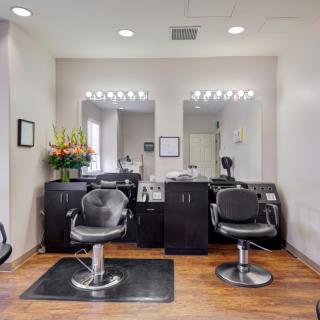 A well-lit hair salon interior featuring two styling chairs and mirrors with vanity lights.