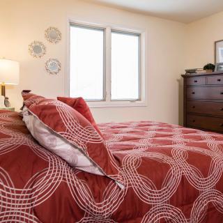 A cozy bedroom with a red and white patterned bedspread, a wooden dresser, and decorative wall plates.
