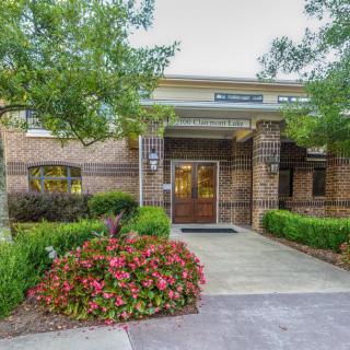 Entrance of a brick building surrounded by well-maintained landscaping with flowers and trees.