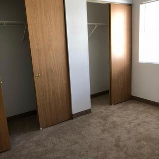 An empty room with a carpeted floor and closets with sliding wooden doors.