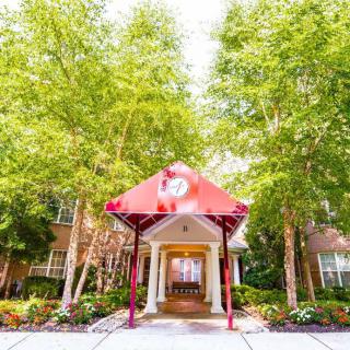 A charming entrance with a red awning surrounded by lush greenery and trees.