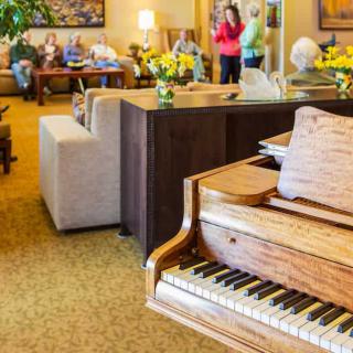 A cozy living room with a grand piano, comfortable seating, and people socializing in the background.