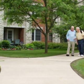 Two seniors walking together on a pathway in a park-like setting.