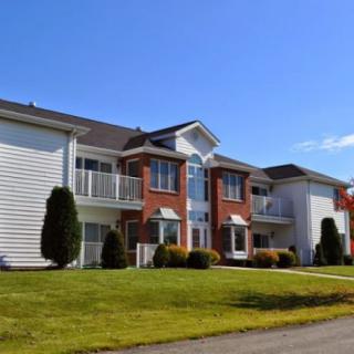 A suburban apartment building with a well-maintained lawn and clear blue sky.