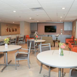 A modern lounge area featuring tables and chairs, with a TV screen and decorative vases on the tables.
