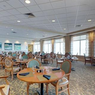 A spacious dining area with neatly arranged tables and chairs, featuring large windows and a carpeted floor.