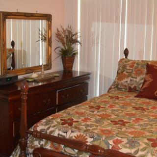 A cozy bedroom featuring a wooden bed with floral bedding, a matching dresser with a mirror, and decorative elements.