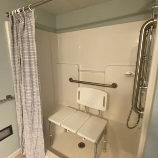 An accessible bathroom with a shower chair and grab bars installed for safety.