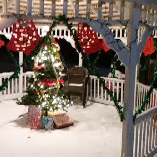 A beautifully decorated gazebo featuring a Christmas tree and holiday decorations, surrounded by snow.