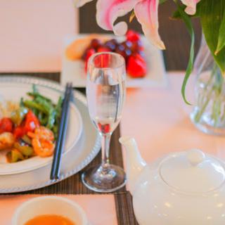 A beautifully arranged dining table featuring Chinese cuisine, a teapot, and fresh fruits alongside elegant floral decor.