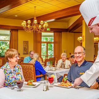 A group of seniors enjoying a meal served by a chef in a restaurant setting.