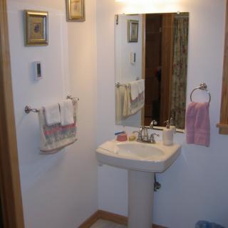 A small bathroom featuring a pedestal sink and a wall-mounted mirror, accompanied by neatly arranged towels and decorative elements.