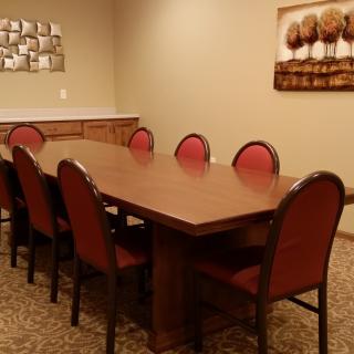A well-furnished conference room with a long meeting table and red upholstered chairs, decorated with wall art.