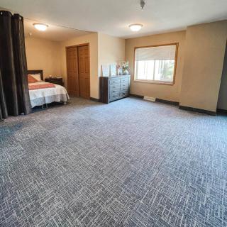 A spacious bedroom with carpeted flooring, a bed, and a dresser.