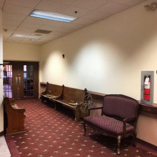 A quiet hallway with benches and a patterned carpet, featuring a wall-mounted fire extinguisher.