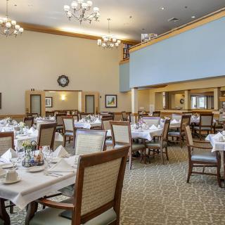 An elegantly set dining room with neatly arranged tables and chairs, featuring chandeliers and a formal atmosphere.