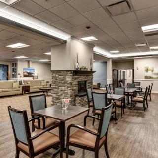 A cozy lounge area with tables, chairs, and a central fireplace, featuring wood flooring and soft lighting.