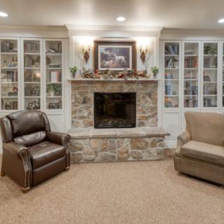 A cozy living room featuring a stone fireplace flanked by glass-fronted bookshelves and comfortable armchairs.