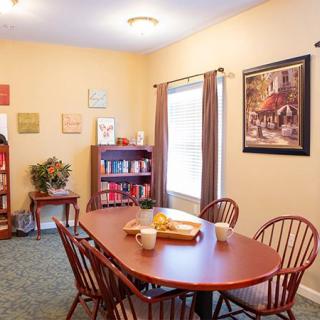 A cozy dining room with a wooden table, surrounded by chairs, a bookshelf with books, and artwork on the walls.