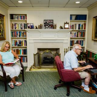 Two people reading in a cozy library with a fireplace.