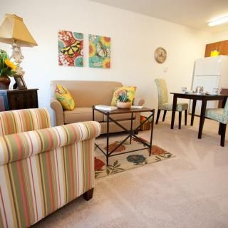 A cozy living space featuring a sofa, armchair, dining area, and colorful artwork on the walls.
