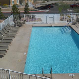 An outdoor swimming pool with surrounding lounge chairs and a safety fence.