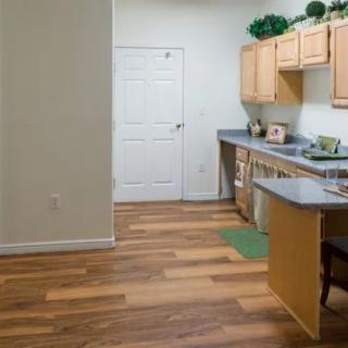 A modern kitchen with wooden flooring, light-colored cabinets, and a sleek countertop.