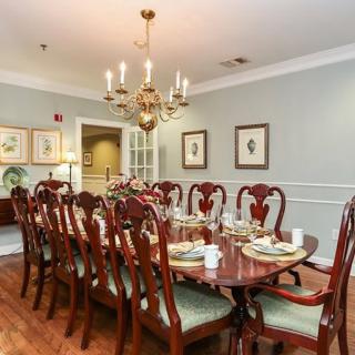 An elegant dining room with a long wooden table set for dinner, featuring a chandelier overhead and decorative wall art.