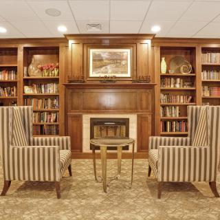 A cozy library interior with bookshelves, a fireplace, and striped armchairs.