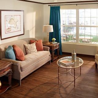 A cozy living room with a sofa, glass coffee table, and large window draped with blue curtains.