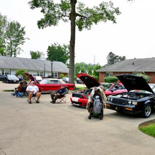 Car enthusiasts working on their vehicles in a parking area.