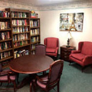 A cozy reading room with a round table, chairs, and bookshelves.