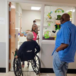 A visitor observing a patient in a wheelchair being attended to by medical staff in a healthcare facility.