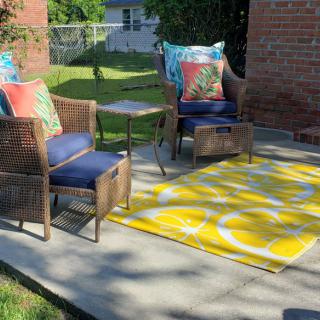 A cozy outdoor patio with wicker chairs, colorful cushions, and a bright yellow rug.