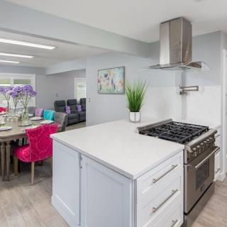 A modern kitchen with a sleek design, featuring a stove and range hood, a white countertop, and a colorful dining area.