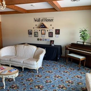 A cozy lounge area featuring a 'Wall of Honor' with photographs, a sofa, and a piano.