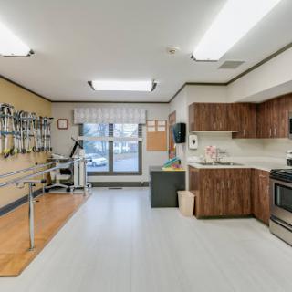 A spacious rehabilitation therapy room equipped with exercise equipment and a kitchenette, designed for patient care.