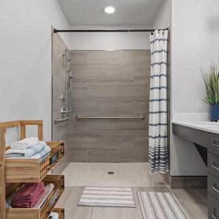 A modern bathroom featuring a walk-in shower with a striped curtain, wooden shelves holding folded towels, and a potted plant on the countertop.