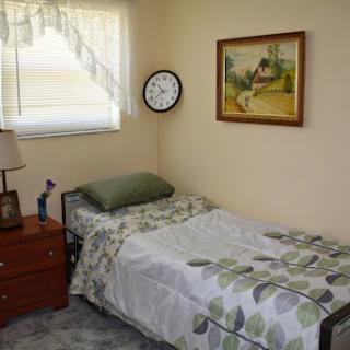 A cozy and simple bedroom featuring a single bed, nightstand, wall clock, and a piece of artwork.